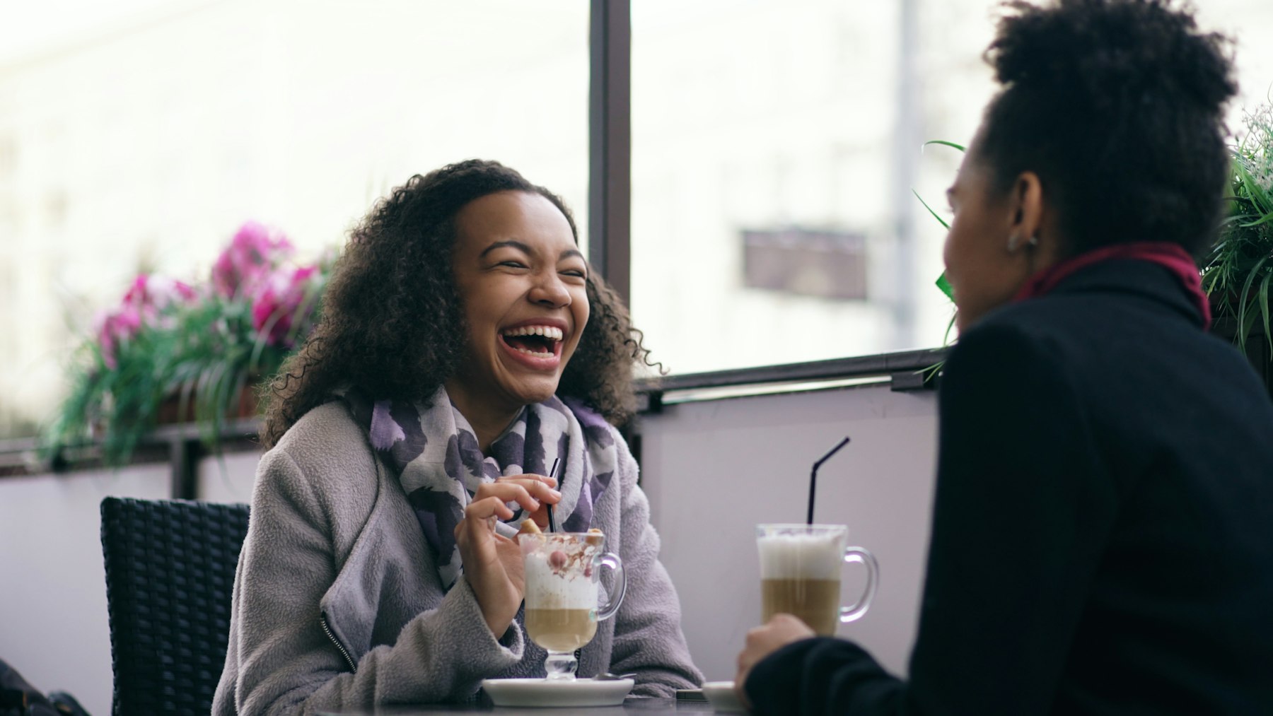 Two friends laughing over coffee at a café table