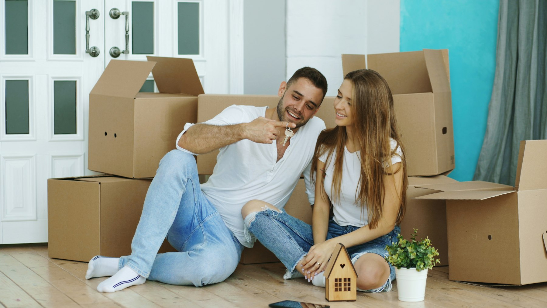 Two people carrying boxes into a bright new apartment
